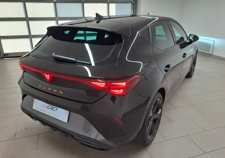 Vue 3/4 arrière droite d'une CUPRA Leon 2025 Noir Minuit avec feux arrière allumés et jantes cuivrées 18 pouces.