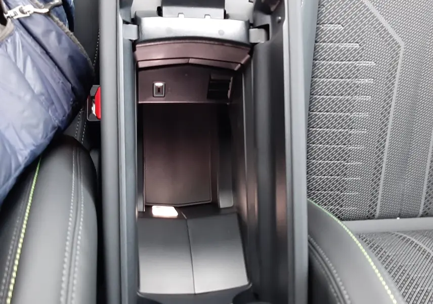 Vue intérieure en plongée du rangement central ouvert de la Peugeot 308 Hybrid 1.2 GT, avec sellerie noire et surpiqûres vertes.