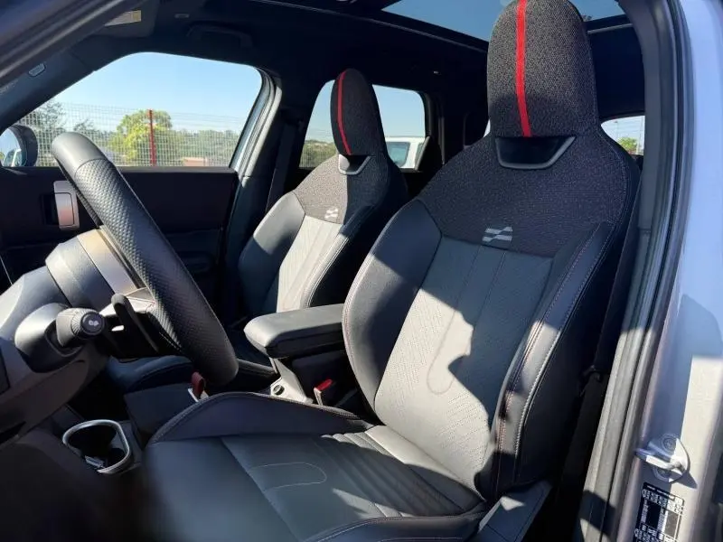 Vue intérieure côté conducteur de la MINI Countryman argentée 2025, sièges sport avec bande rouge et tissu texturé.