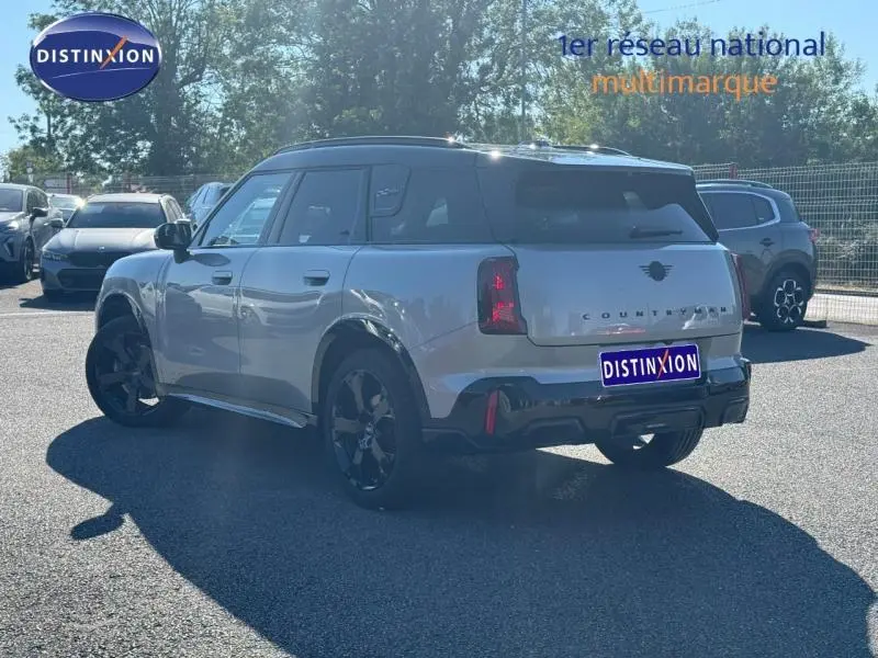 Vue 3/4 arrière droite d'un MINI Countryman argenté avec toit noir et jantes noires sur parking extérieur.
