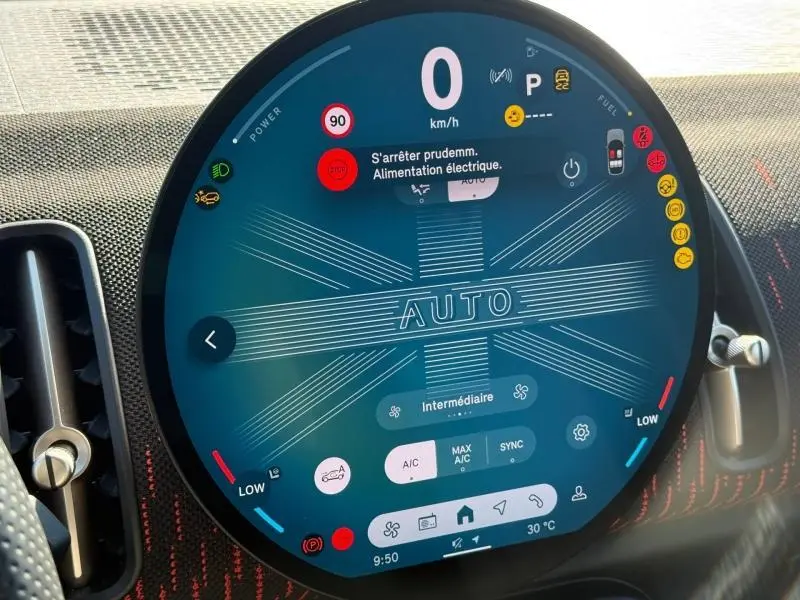 Gros plan sur l'écran tactile circulaire du tableau de bord du MINI Countryman argenté, affichant les réglages climatiques et alertes.