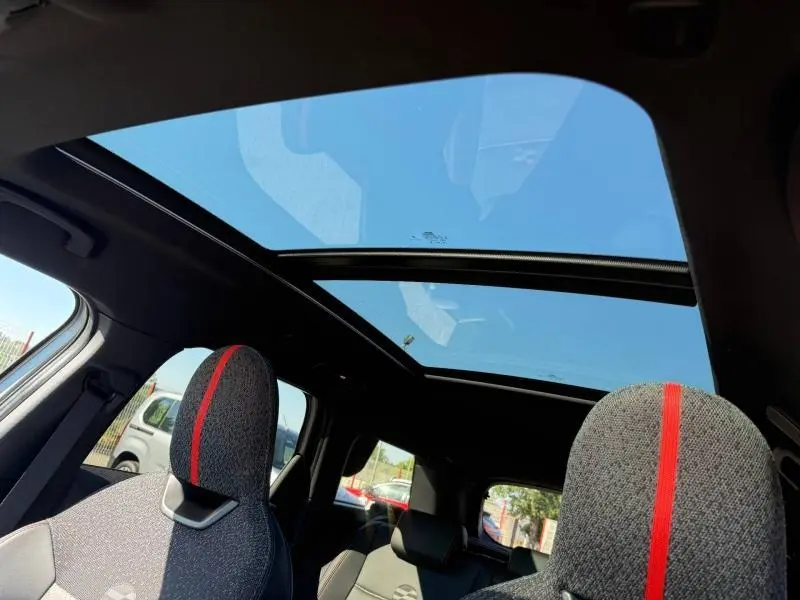 Vue intérieure du MINI Countryman argenté 2025, mettant en valeur le toit panoramique et les sièges avant avec bande rouge centrale.