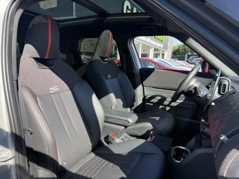 Vue intérieure côté conducteur du MINI Countryman argenté 2025, sièges sport noirs avec surpiqûres rouges et toit panoramique.
