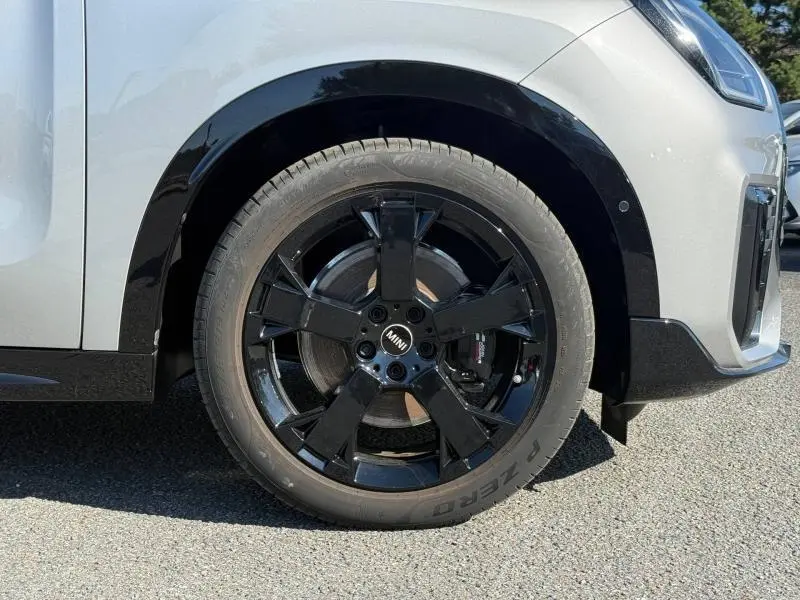 Gros plan sur la roue avant droite noire brillante d’un MINI Countryman argenté, avec jante alu et étrier visible.