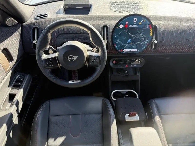 Vue intérieure avant du MINI Countryman argenté 2025, volant multifonctions et écran tactile circulaire central avec navigation.