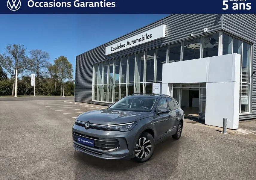 Volkswagen Tiguan gris en 3/4 avant droit, avec jantes alliage noir brillant, devant un bâtiment de concession.