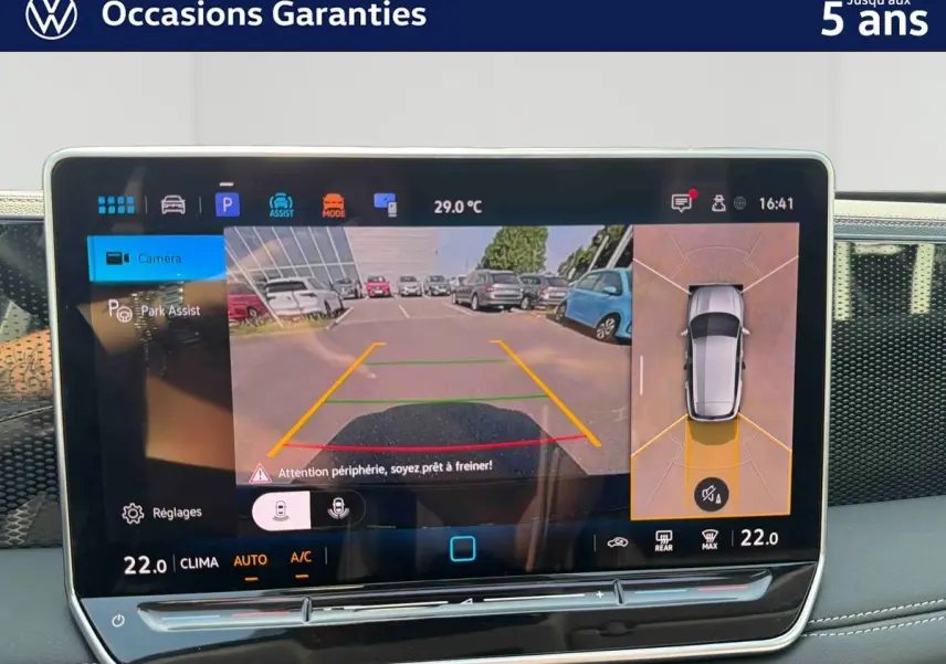 Écran tactile intérieur montrant l'aide au stationnement avec vue caméra arrière et angles morts du Volkswagen Tiguan gris.