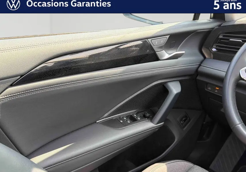 Détail de la porte avant gauche grise du Volkswagen Tiguan 2025 avec commandes électriques et insert décoratif noir brillant.