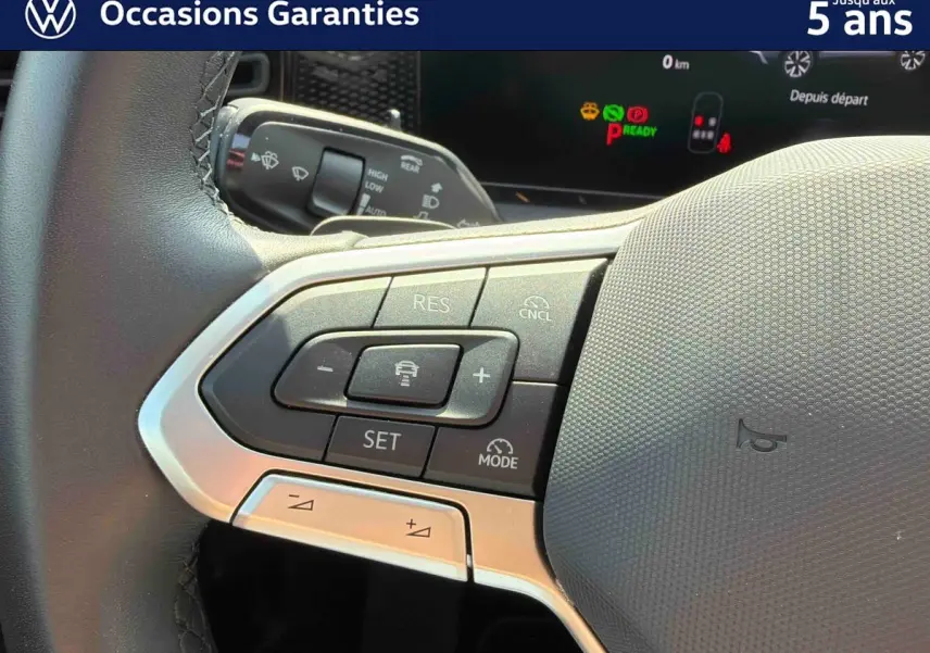 Gros plan sur le volant multifonction cuir du Volkswagen Tiguan gris, avec commandes de régulateur de vitesse visibles.