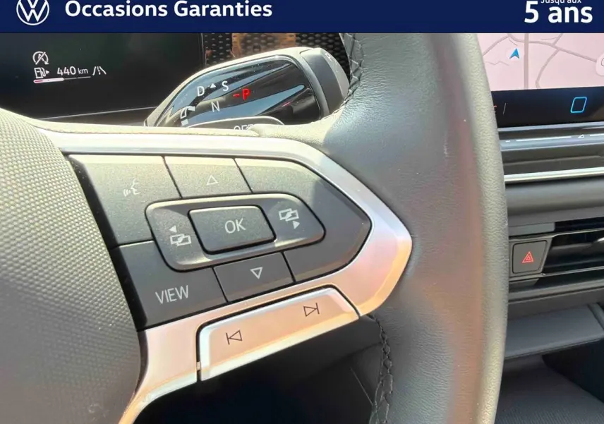 Gros plan sur les commandes multifonctions à gauche du volant cuir du Volkswagen Tiguan gris, avec écran tactile en arrière-plan.