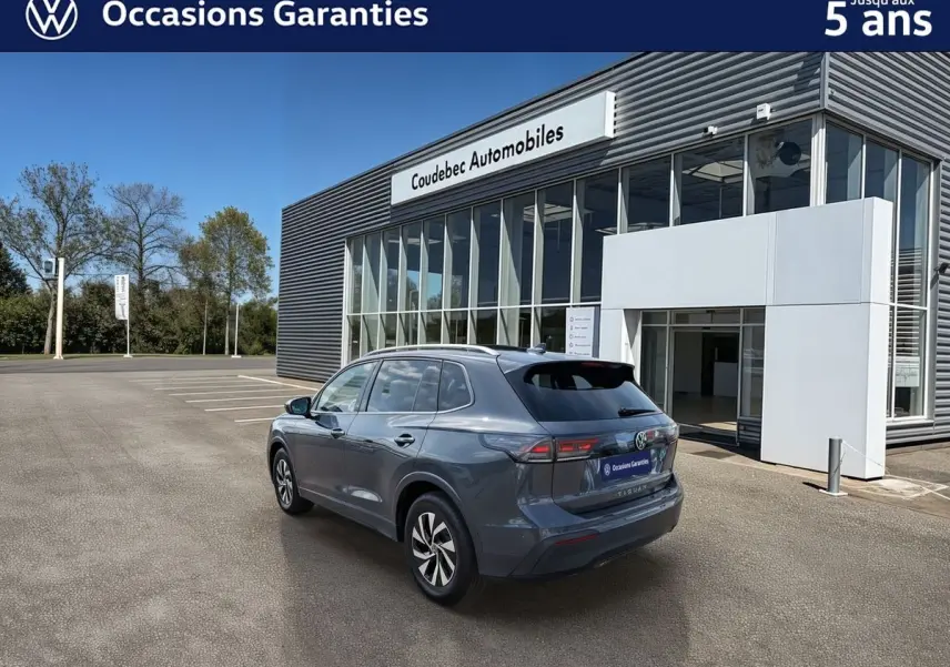 Volkswagen Tiguan gris vu en 3/4 arrière droit devant un bâtiment de concession Coudebec Automobiles.