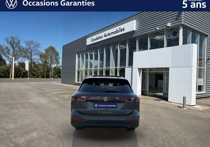 Vue arrière d’un Volkswagen Tiguan gris 2025 garé devant un bâtiment moderne avec vitres et enseigne Coudebec Automobiles.