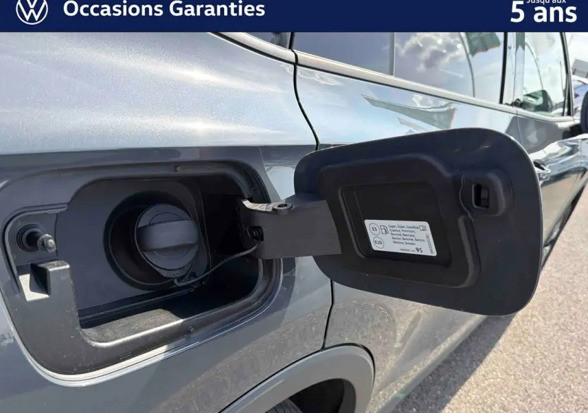 Vue rapprochée de la trappe à carburant ouverte côté gauche d’un Volkswagen Tiguan gris 2025, détails du bouchon visibles.