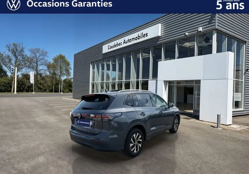 Vue 3/4 arrière droite d'un Volkswagen Tiguan gris avec jantes alliage noir devant un bâtiment moderne.