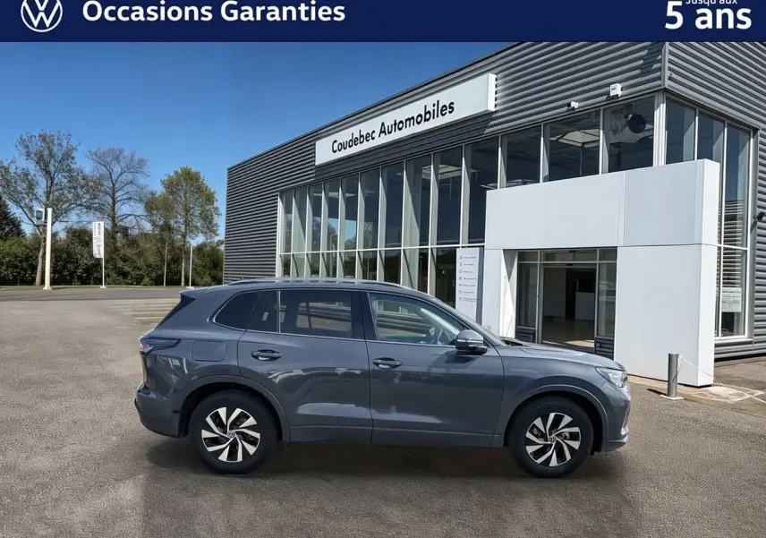 Volkswagen Tiguan gris vu de profil côté gauche, avec jantes alliage noir brillant, devant un bâtiment moderne.