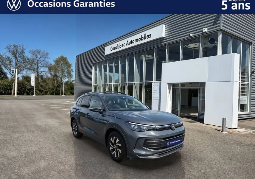 Volkswagen Tiguan gris vu en 3/4 avant droit, avec jantes alliage noir brillant, devant un showroom moderne.