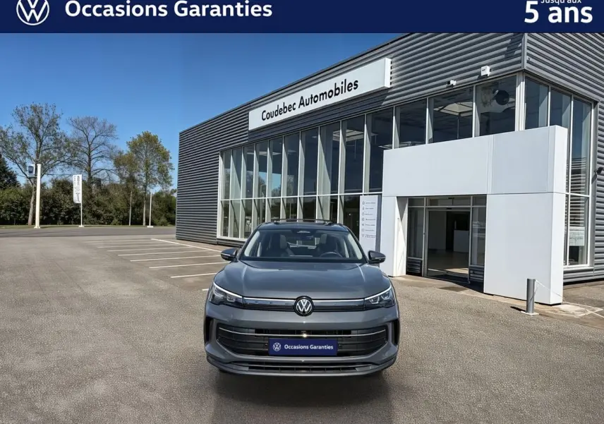 Volkswagen Tiguan gris vu de face, avec calandre épurée et phares LED, devant un bâtiment moderne de concession.