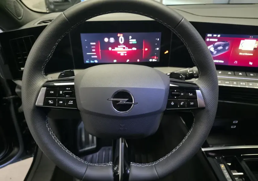 Vue rapprochée du volant noir perforé de l’Opel Astra Hybrid 2024 avec tableau de bord digital et écran tactile.