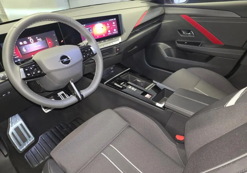 Vue intérieure côté conducteur de l’Opel Astra Hybrid 2024 noire, avec tableau de bord digital et touches rouges décoratives.