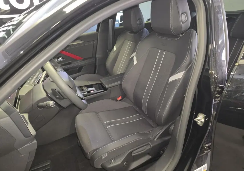 Vue intérieure côté conducteur de l’Opel Astra Hybrid 2024 noire, sièges tissu/TEP avec surpiqûres blanches et accoudoir central.