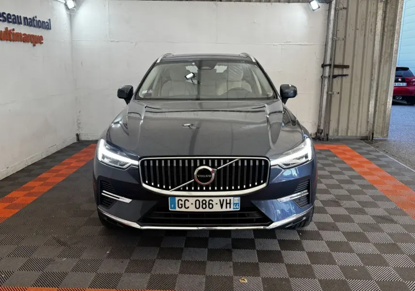 Vue frontale d'un Volvo XC60 bleu avec calandre verticale chromée et phares LED allumés dans un garage.