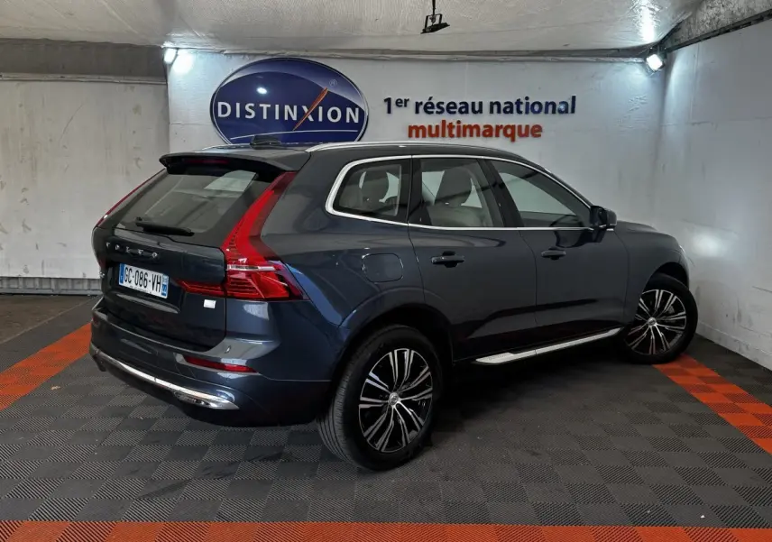 Vue 3/4 arrière droite d'un Volvo XC60 bleu hybride rechargeable avec jantes noires et toit noir dans un garage.