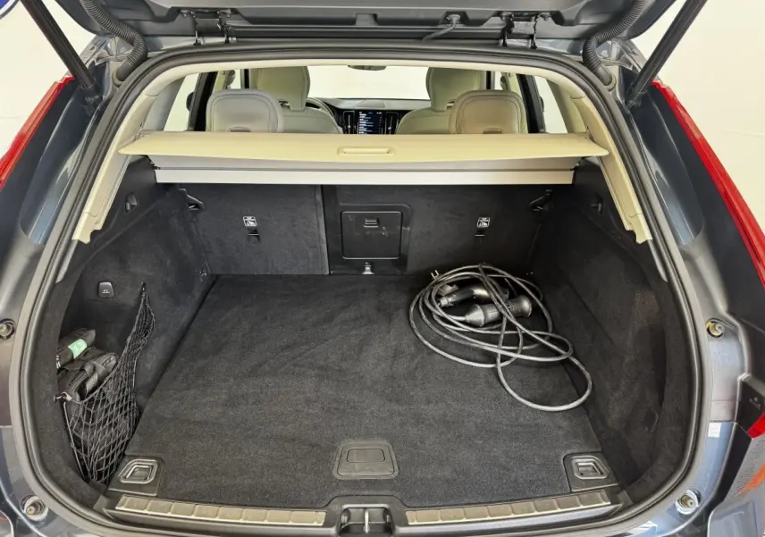 Coffre ouvert vu de l'arrière d'un Volvo XC60 bleu, avec câble de recharge hybride visible sur le tapis noir.
