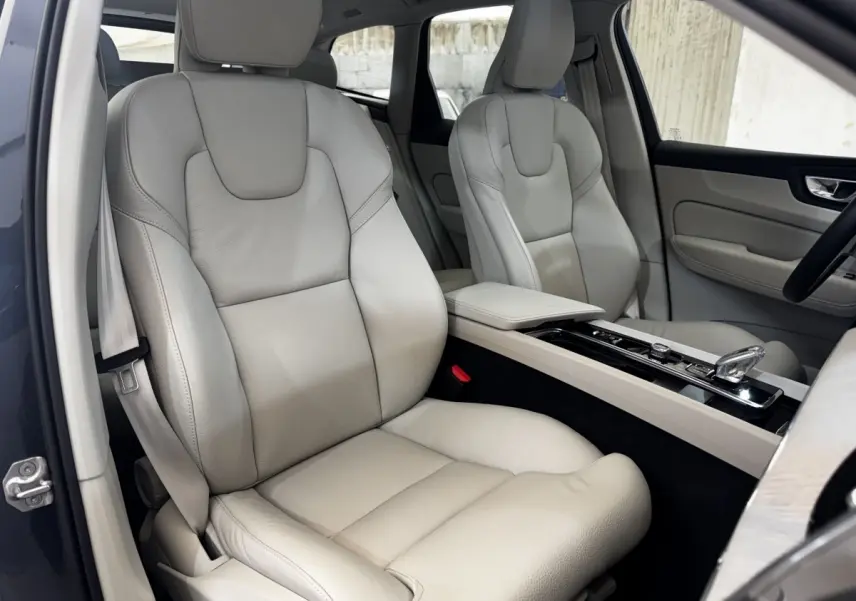 Vue intérieure côté conducteur du Volvo XC60 bleu, sièges avant en cuir beige avec console centrale élégante.