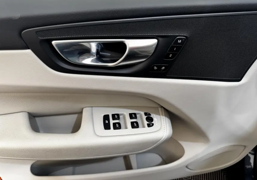 Détail de la porte côté conducteur du Volvo XC60 bleu 2021, avec commandes de vitres et poignée chrome.