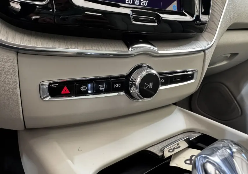 Gros plan sur la console centrale beige du Volvo XC60 bleu, avec commandes multimédia et climatisation visibles.