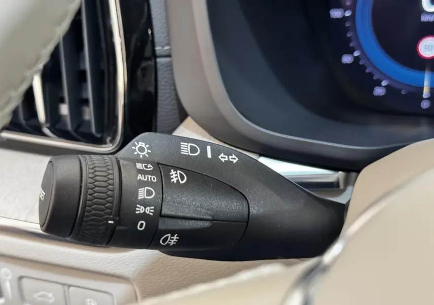 Gros plan sur la commande des phares et clignotants du tableau de bord beige du Volvo XC60 bleu hybride rechargeable.