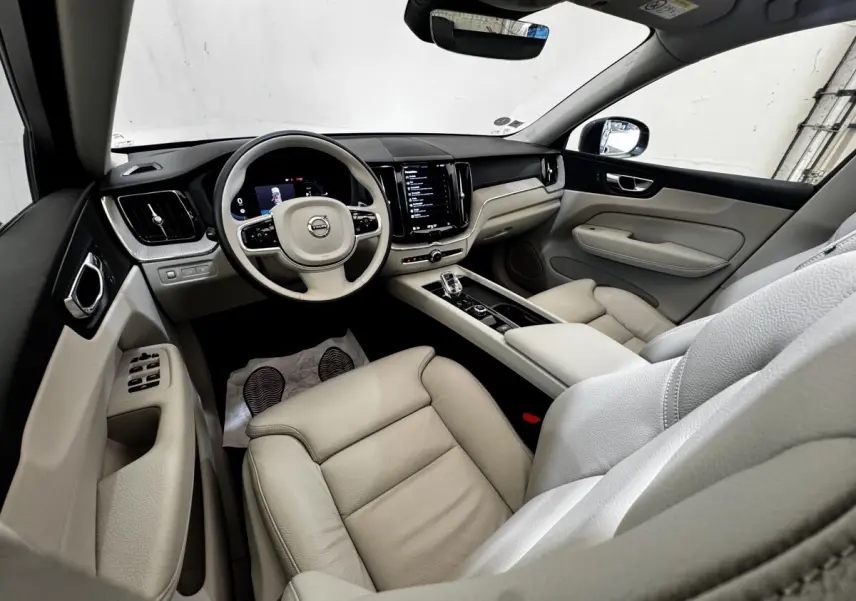 Intérieur beige clair du Volvo XC60 Recharge T8 vu côté conducteur, avec tableau de bord numérique et écran tactile central.