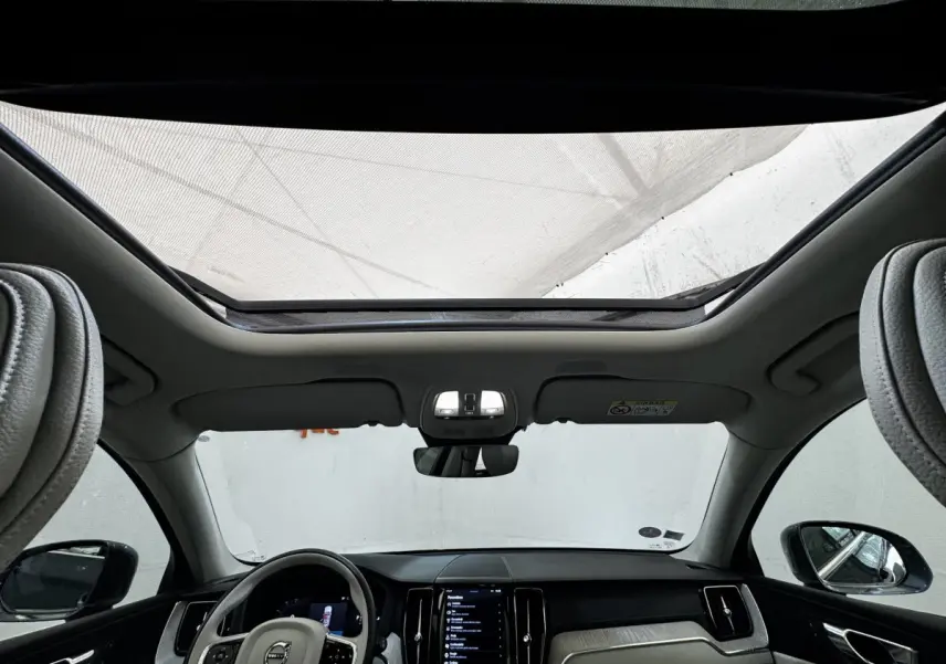 Vue intérieure avant du Volvo XC60 bleu, montrant le toit ouvrant panoramique et le tableau de bord moderne noir et beige.