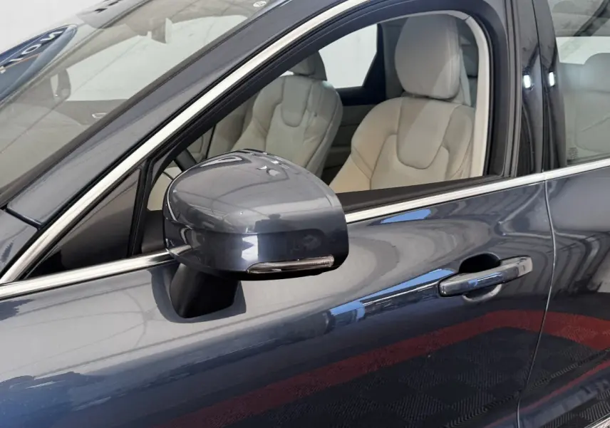 Gros plan sur le rétroviseur et la portière côté conducteur d’un Volvo XC60 bleu avec intérieur cuir beige.