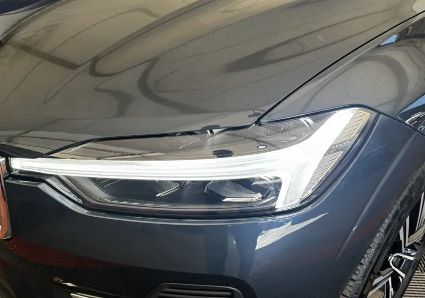 Gros plan sur le phare avant droit allumé d’un Volvo XC60 bleu hybride rechargeable, soulignant ses lignes modernes.