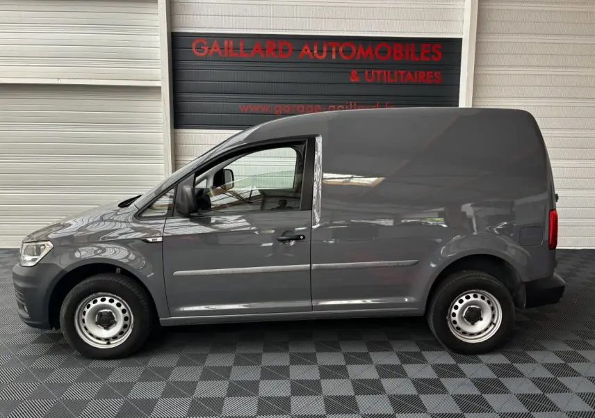 Profil côté gauche d'un utilitaire Volkswagen Caddy gris foncé 2019 avec porte latérale pleine et jantes acier simples.