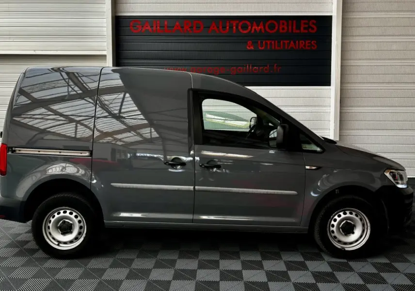 Profil côté gauche d'un utilitaire Volkswagen Caddy gris foncé 2019 avec portes coulissantes et jantes acier simples.