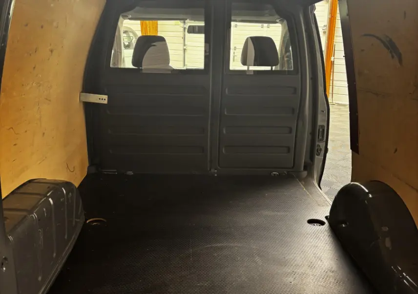 Vue intérieure arrière du Volkswagen Caddy gris foncé 2019, montrant l'espace de chargement avec cloison pleine en bois.