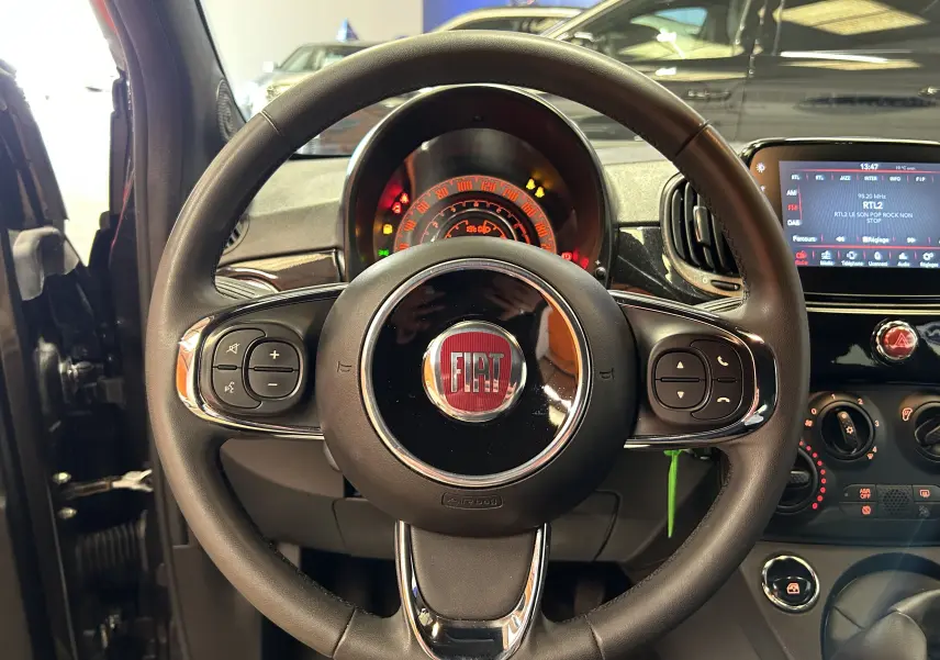 Vue rapprochée du volant noir de la Fiat 500 2023 avec tableau de bord et écran tactile en arrière-plan.