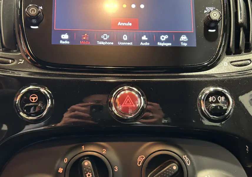 Gros plan sur la console centrale noire de la Fiat 500 2023, avec écran tactile et commandes climatisation visibles.