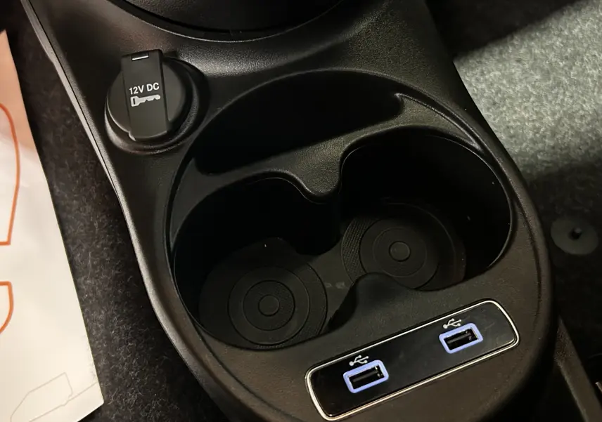Gros plan sur la console centrale noire de la Fiat 500 2023 avec porte-gobelets et deux ports USB bleus.
