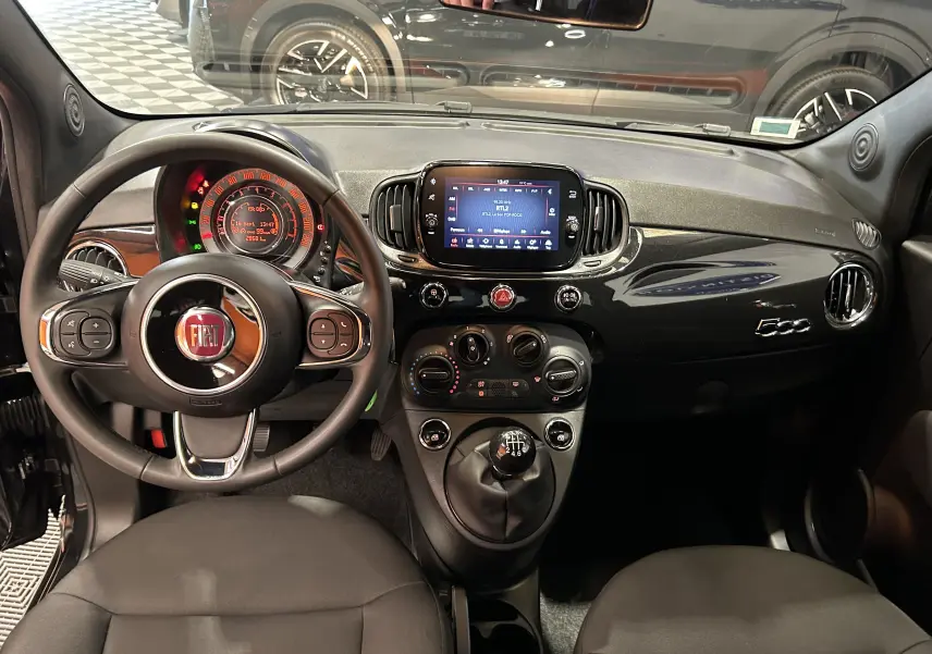 Vue intérieure avant de la Fiat 500 noire 2023, tableau de bord avec écran tactile et volant multifonction.