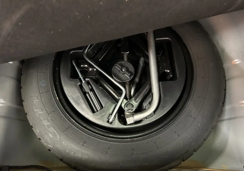 Gros plan sur la roue de secours et les outils de bord du coffre d'une FIAT 500 noire 2023.