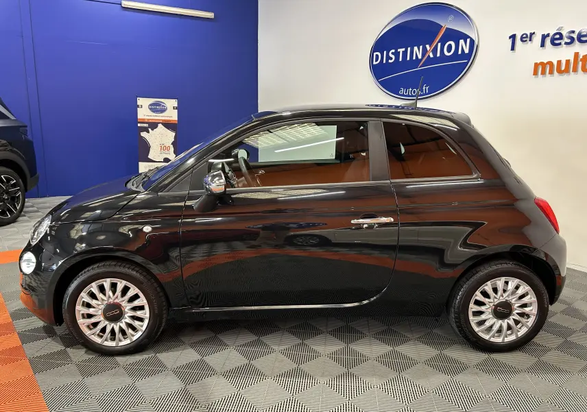 Profil côté gauche d'une FIAT 500 noire 2023 en intérieur, mettant en valeur ses jantes élégantes et sa silhouette compacte.