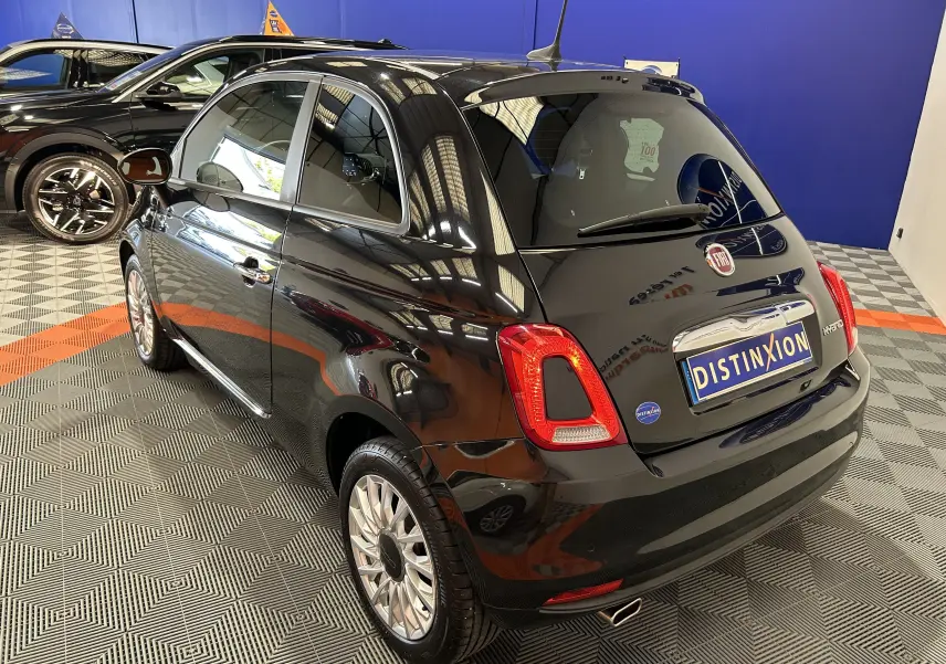 Vue 3/4 arrière droite d'une FIAT 500 noire 2023 avec radar de recul, sur sol damier en intérieur showroom.