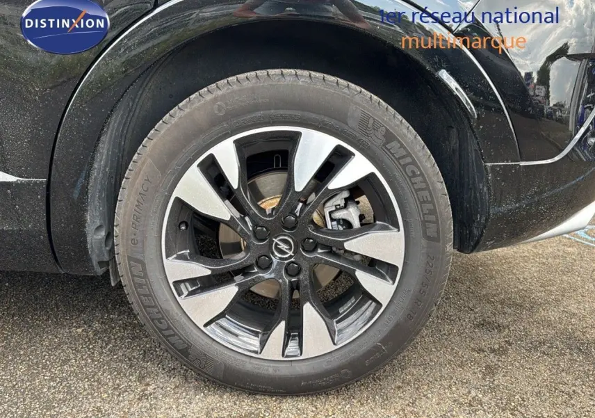 Gros plan sur la roue avant droite noire de l'Opel Grandland 1.6 Turbo Hybrid 225ch GS avec jante bi-ton et logo Opel.