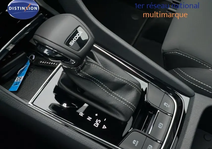 Gros plan sur le levier de vitesses automatique noir avec logo SKODA, entouré de commandes sur la console centrale intérieure.