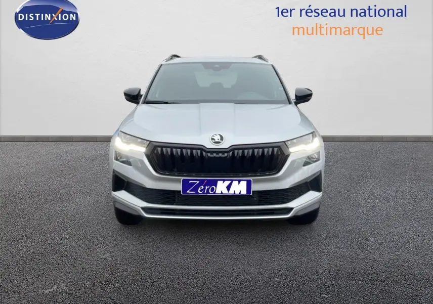 Vue frontale d'un Skoda Karoq gris argent métallisé 2025 avec calandre noire et phares allumés.