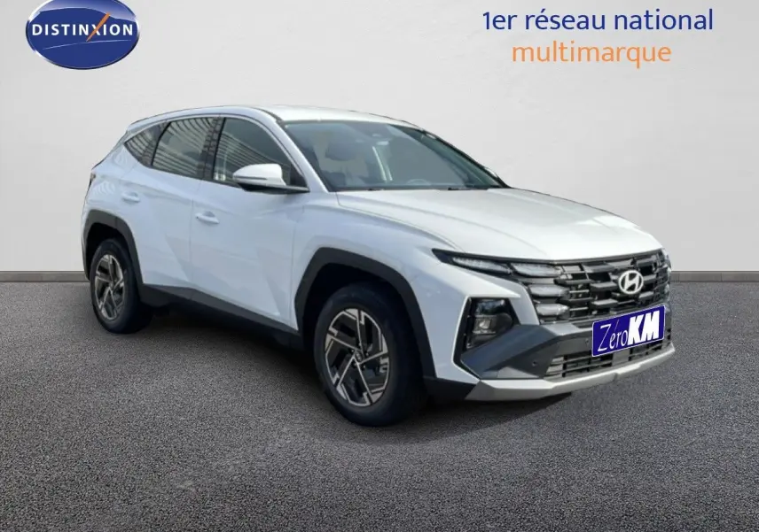 Hyundai Tucson blanc Atlas en 3/4 avant droit, avec calandre noire et jantes bi-ton visibles.