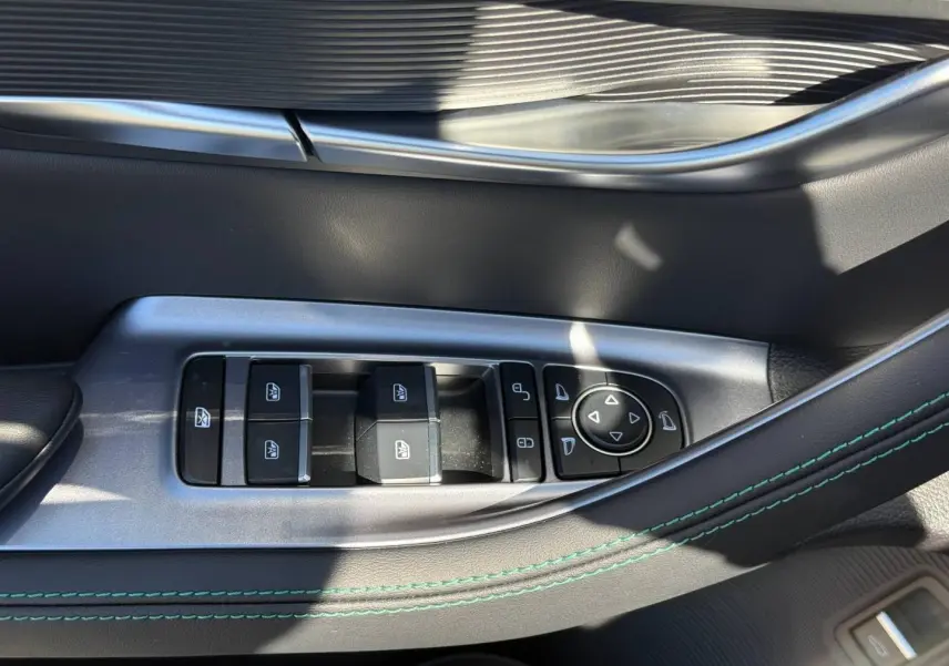 Gros plan sur la commande des vitres électriques côté conducteur du BYD SEAL U 1.5 DM-i en intérieur noir avec surpiqûres vertes.